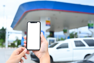 Close up shot of woman holding smartphone with blank screen on the background of a gas station