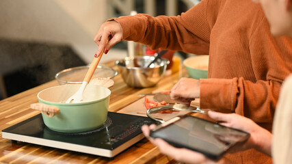 Young couple cooking together in their kitchen and following a recipe on digital tablet
