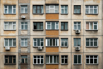 Fototapeta premium Facade of an old apartment building with multiple windows and air conditioning units. The building shows weathering and varying window styles.