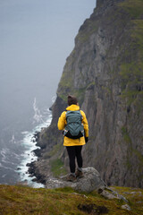 An adventurous female stands at a cliffs edge, surrounded by a stunning, misty landscape.