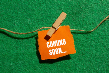 Coming soon message written on ripped torn orange paper piece with green background. Conceptual...