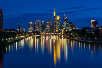 Photo from Deutschherren Bridge in Frankfurt after sunset in blue hour. The city center and the river Main are lit in the background.