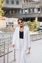 Obraz premium Stylish Woman in Striped Suit and Sunglasses Walking Outdoors