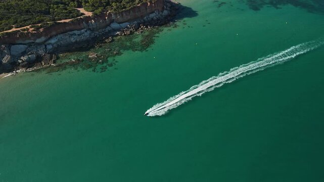 Jet ski seen from the sky near the mediterranean coast. Jet ski leaves a trail of white foam tracing a diagonal in the plane. Drone flight