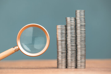 Magnifying glass and very high coins stacks, check the good finance status and income, high return investment