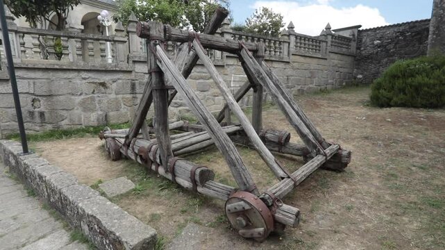 Ancient wooden catapult displayed outdoors on stone courtyard of historic structure