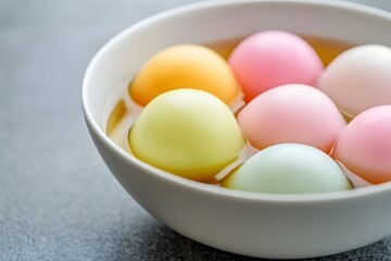 Close-up of colorful Tangyuan in clear syrup inside a white ceramic bowl on a gray table