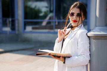 Confident Businesswoman in Stylish Attire Holding a Notebook with a Modern Urban Background