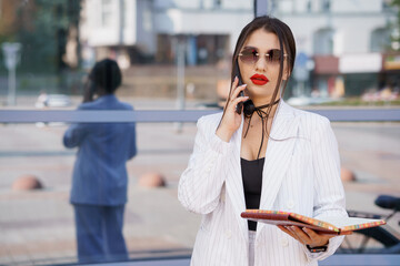 Stylish Businesswoman Engaged in a Phone Conversation While Holding a Notebook