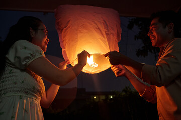 Obraz premium Happy Asian couple launching lantern outdoors and celebrating holiday