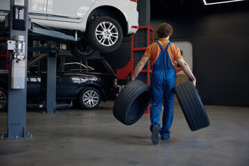 Full-length shot of male auto mechanic carrying car tires © Nomad_Soul