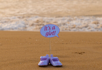 It's a boy and it's a girl baby written text announcement on the beach sand with shoe. Clean sea water and small beach waves are in background