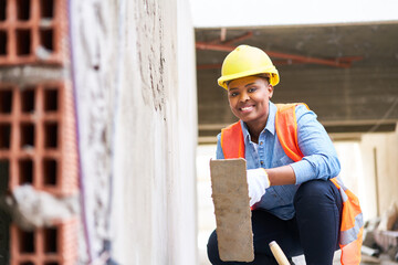 Full length portrait of happy young female labor with trowel crouching on plank by wall at...