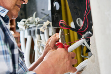 Senior male electrician using pliers while fixing wires at incomplete house construction site