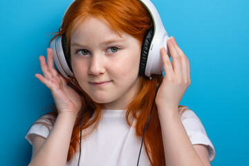 A girl in blue and white is playing with headphones the . happy female w concept. a girl with headphones on her head on a blue . a girl in blue with headphones on her head and music on lifestyle the.