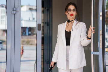 Elegant Woman in Fashionable White Suit with Sunglasses at Doorway