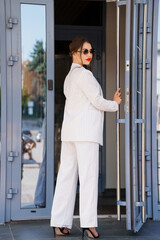 Elegant Businesswoman in Chic Striped Suit Exiting Modern Office Entrance with Confidence