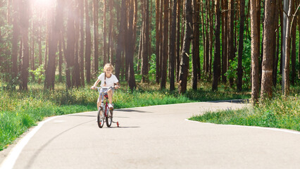 Child riding a bike in summer park. Children learning to drive a bicycle on a driveway outside. Kid riding bike. Child on bicycle, bike outdoor.