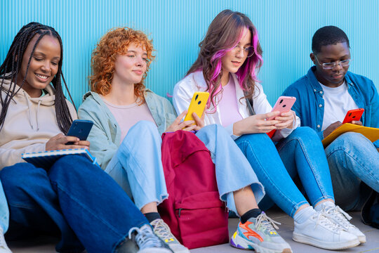 A group of diverse young people sitting outdoors using smartphones and notebooks