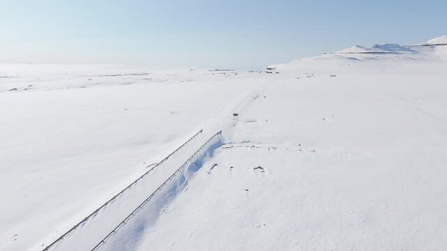 Slow aerial flight across untouched snowy landscape in Lesotho, Africa, over Sani Top village, border post, and along cliff edge of Sani Pass to reveal snowy mountain landscape in South Africa below