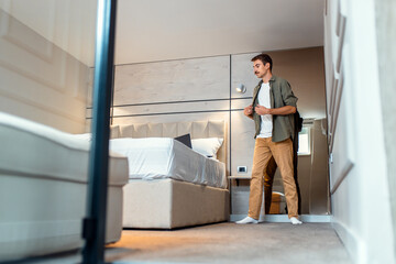 Fototapeta premium Man standing next to the bed in bedroom using laptop.