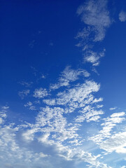 A serene sky, painted in shades of deep blue, is adorned with fluffy white clouds that drift gracefully across the expanse. The scene evokes feelings of peace and tranquility.