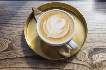 Cappuccino with Heart Latte Art on Wooden Table in Golden Saucer at Cafe