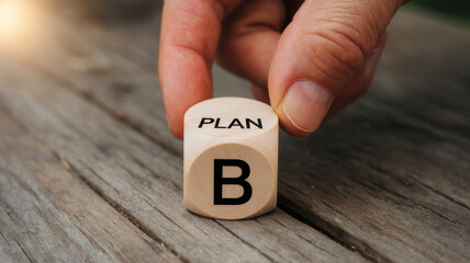 Hand holding a wooden block with the text PLAN B on a rustic wooden surface.