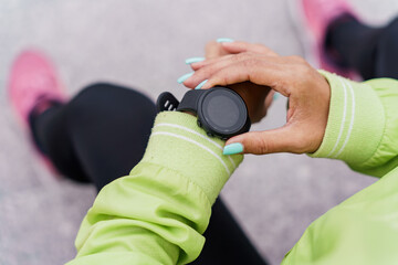 A Person Checks a Fitness Watch While Wearing a Green Jacket and Pink Sneakers During an Outdoor...