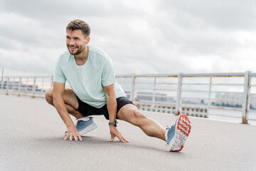 A Man Performing a Dynamic Stretching Exercise Outdoors on a Cloudy Day Near a Waterfront