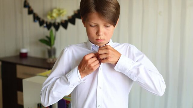 a teenage boy is shown in a close up as he prepares to wear a white school shirt. He carefully unbuttons the shirt and slides it over his arms. Moment in a teenager daily life