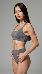 Fototapeta premium European fitness model showcasing toned arms in a grey athleisure outfit against a tranquil light-gray backdrop