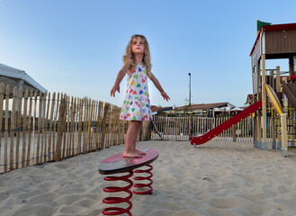 Little girl having fun on a beach playground at sunset time
