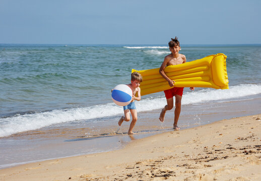 Sunny beach joy: kids are running with floaties and a beachball