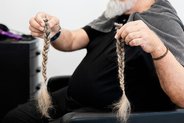 Elderly man holding braided hair for donation