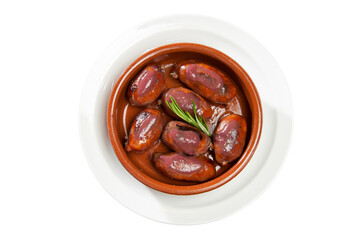 Overhead shot of a small casserole dish on a white plate with blood sausages and rosemary on a white background