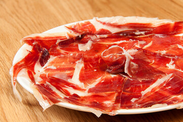 Fragment of plate with slices of Serrano ham in circular formation on wooden background