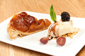 Ensaimada with peach compote and scoop of vanilla ice cream with berries and crunchy on a white plate with a wooden background