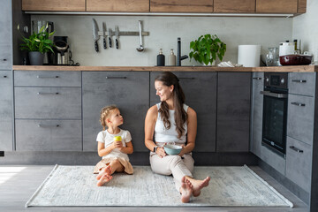 Mother and daughter sitting on kitchen floor, eating or having a breakfast and playing. Family bonding