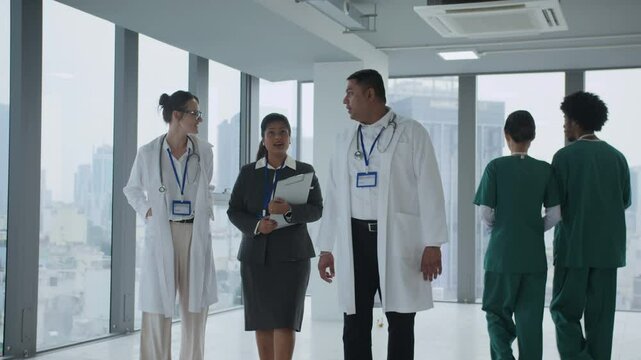 Tracking slow motion shot of multiracial medical coworkers talking while walking along hall of modern hospital