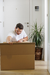 Young man moves into his new house. He is single and a homeowner. New beginnings. Plants in the home. Opening cardboard boxes for moving. Mortgage concept. Paying rent. New tenant.