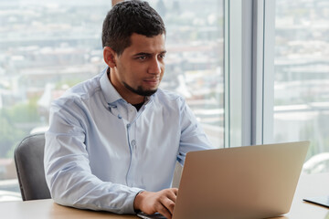 Fototapeta premium Man is working on his laptop at desk. office technology computer concept. man is sitting at table with laptop. a man is sitting at a desk with a laptop and a lifestyle table for business.