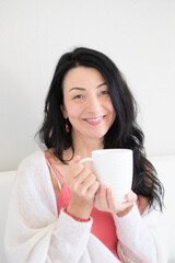 Woman with Long Dark Hair Holding White Mug Smiling Joyfully in Casual Light Room Cozy Lifestyle Concept