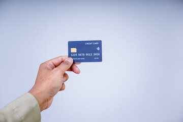 A hand holding a modern credit card with a microchip against a plain background.