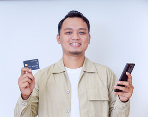 A cheerful man holding a smartphone and credit card, ready for a transaction.