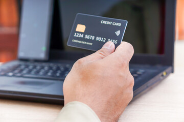 A person holds a credit card in front of a laptop, indicating online transactions.
