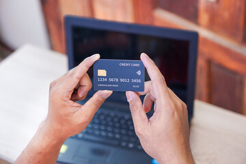 A person holds a credit card in front of a laptop, indicating online transactions.