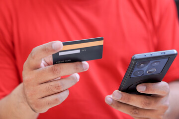 A person with red t-shirt holding a credit card in one hand and a smartphone