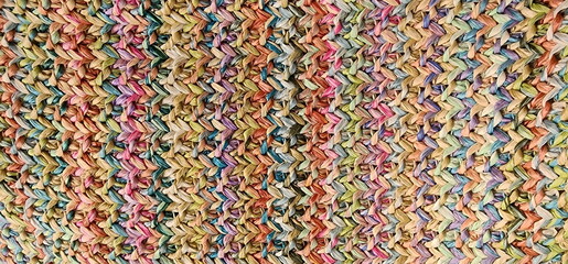 Obraz premium Beautiful patterns of handicrafts from ropes and crochet hooks. Close-up of the pattern on a handmade bag woven from colorful plastic strings. Multi-colored crochet work suitable for clothing. 