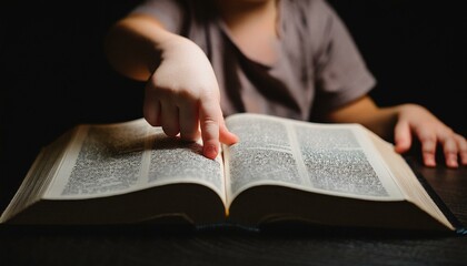 Fototapeta premium A child's small hand touching the center of an open Bible
